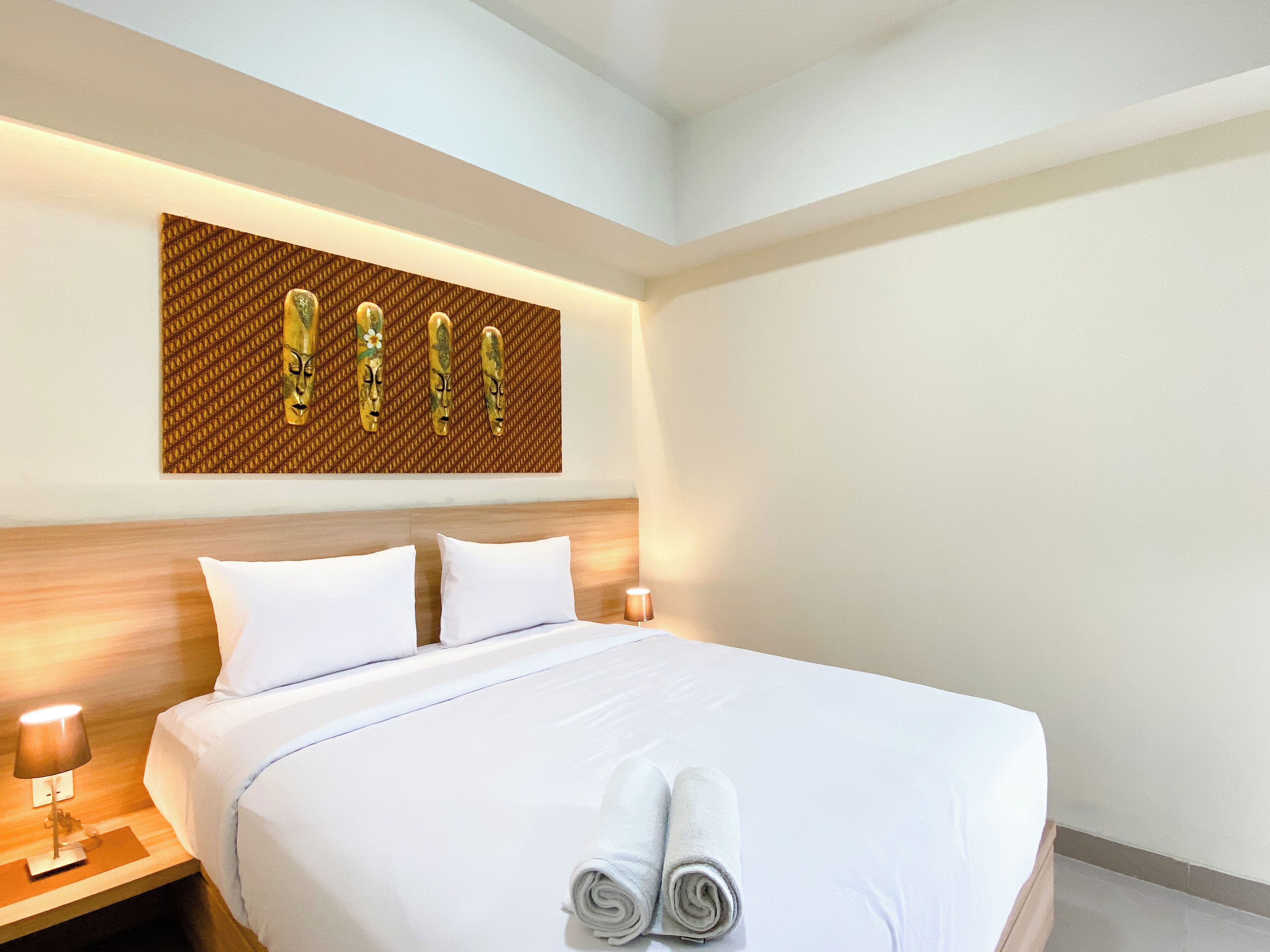 Una camera d'albergo con un letto grande, lenzuola bianche, una testiera con pannello in legno e un'opera d'arte appesa al muro sopra il letto.