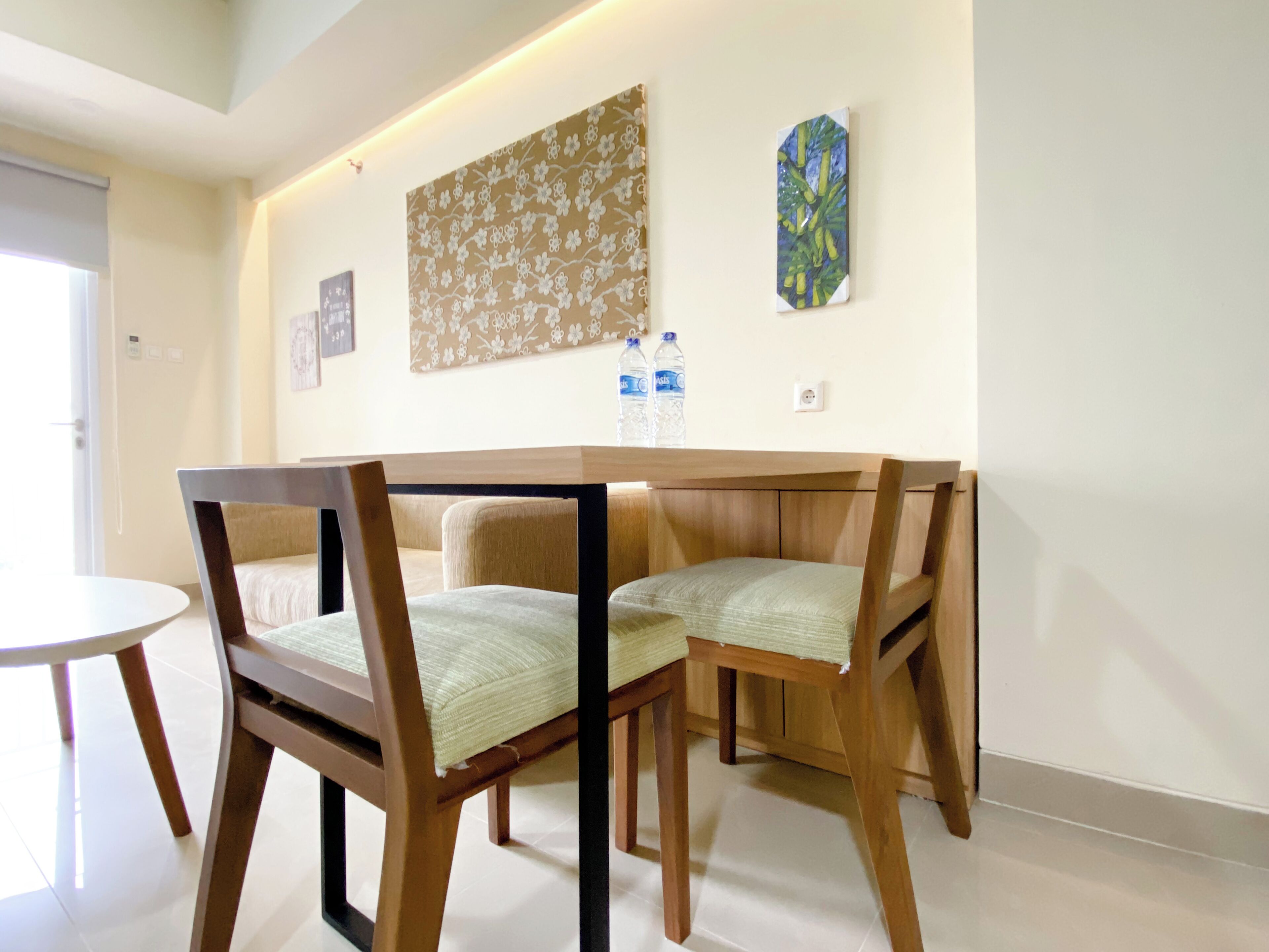 Un coin repas avec une table et des chaises en bois, une décoration murale à motifs floraux et deux bouteilles d’eau accrochées au mur.