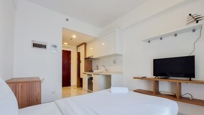 Una habitación de hotel con una cama, un escritorio de madera, un televisor y una kitchenette.