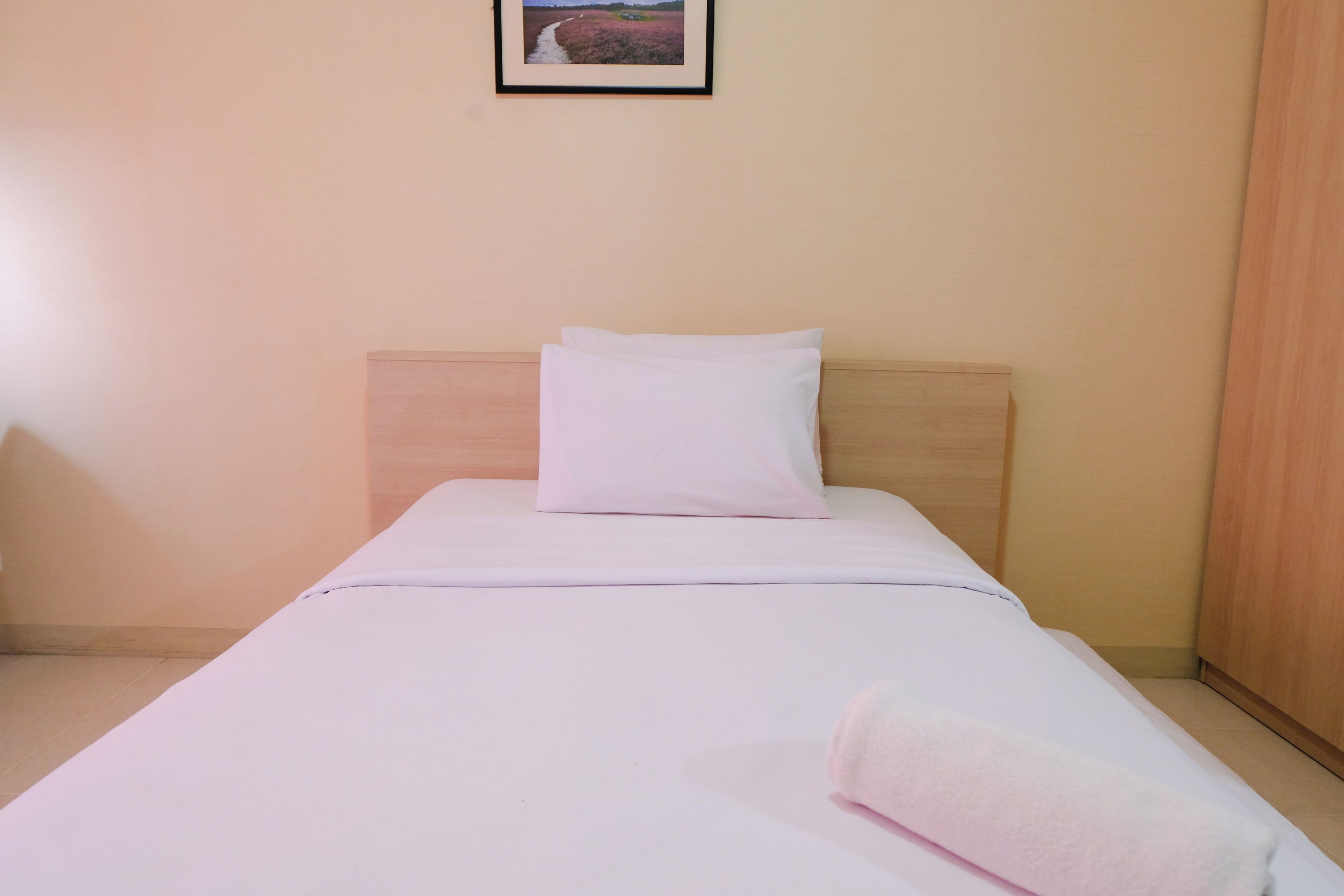 A neatly made bed with white bedding and pillows, a wooden headboard, and a framed picture on the wall.