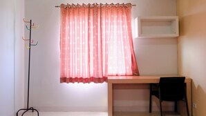 Una habitación con escritorio, silla, perchero y ventana con cortina.