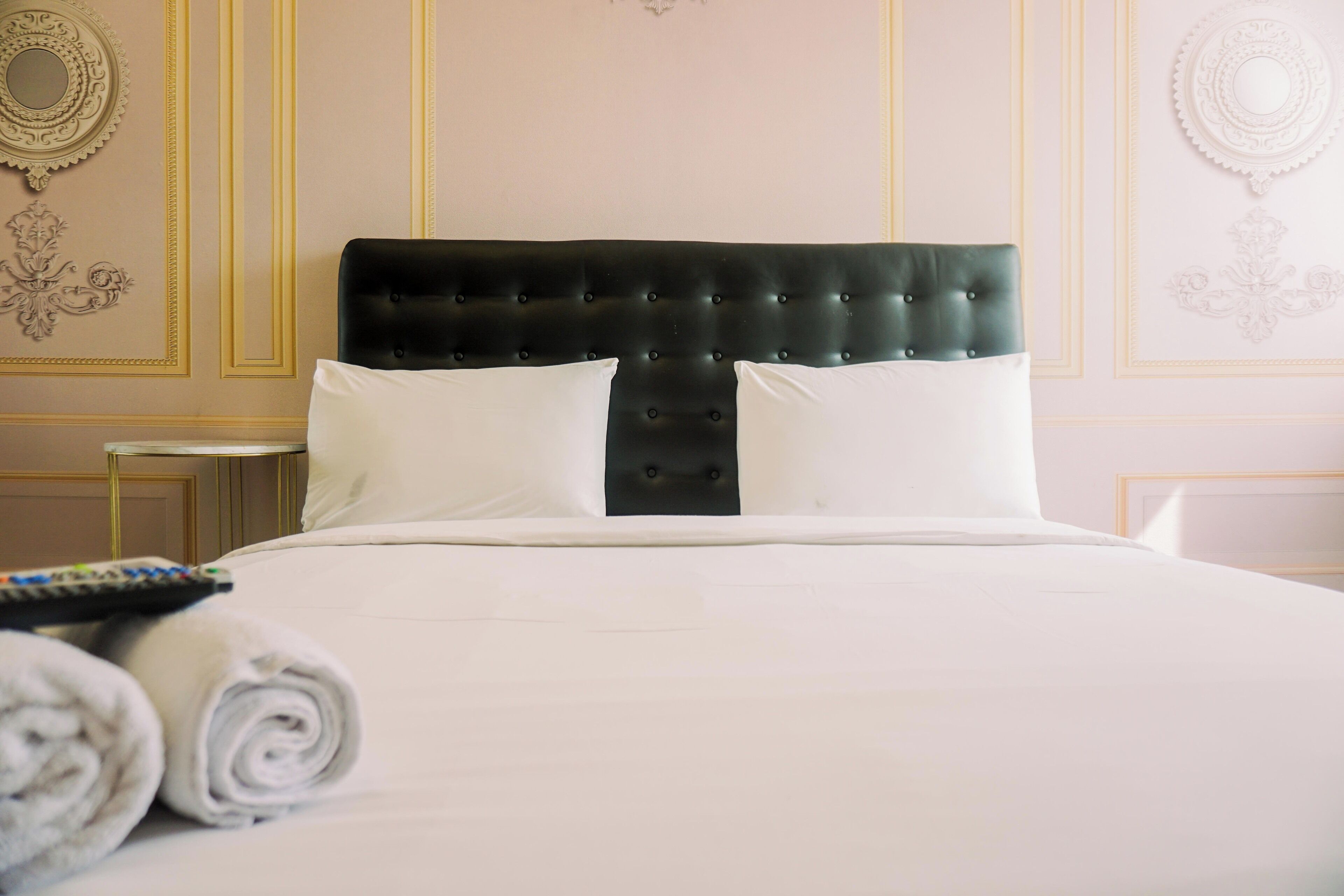 A neatly made bed with a black headboard, white pillows, and rolled towels on the side.