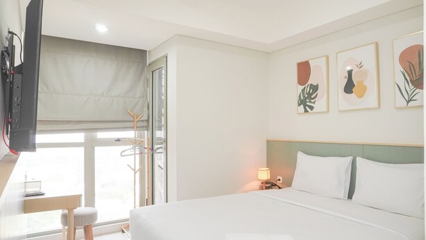 Une chambre d’hôtel avec un lit, un bureau équipé d’un ordinateur, une télévision et des œuvres d’art accrochées au mur.