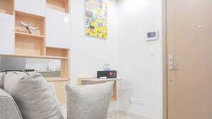 Une chambre d’hôtel moderne avec un canapé gris, une petite table sur laquelle se trouve une bouteille d’eau, une télévision et une affiche colorée de dessin animé accrochée au mur.