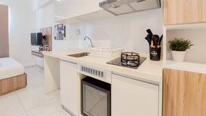 Una cuina moderna amb armaris blancs, un rentaplats integrat, una campana extractora d'acer inoxidable i un taulell amb un rentatall i una petita planta.