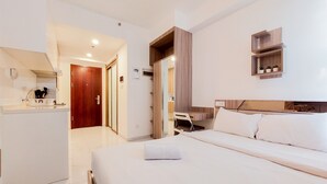 Una habitació d'hotel amb llit, escriptori, cadira, mirall i una petita estant amb plantes.
