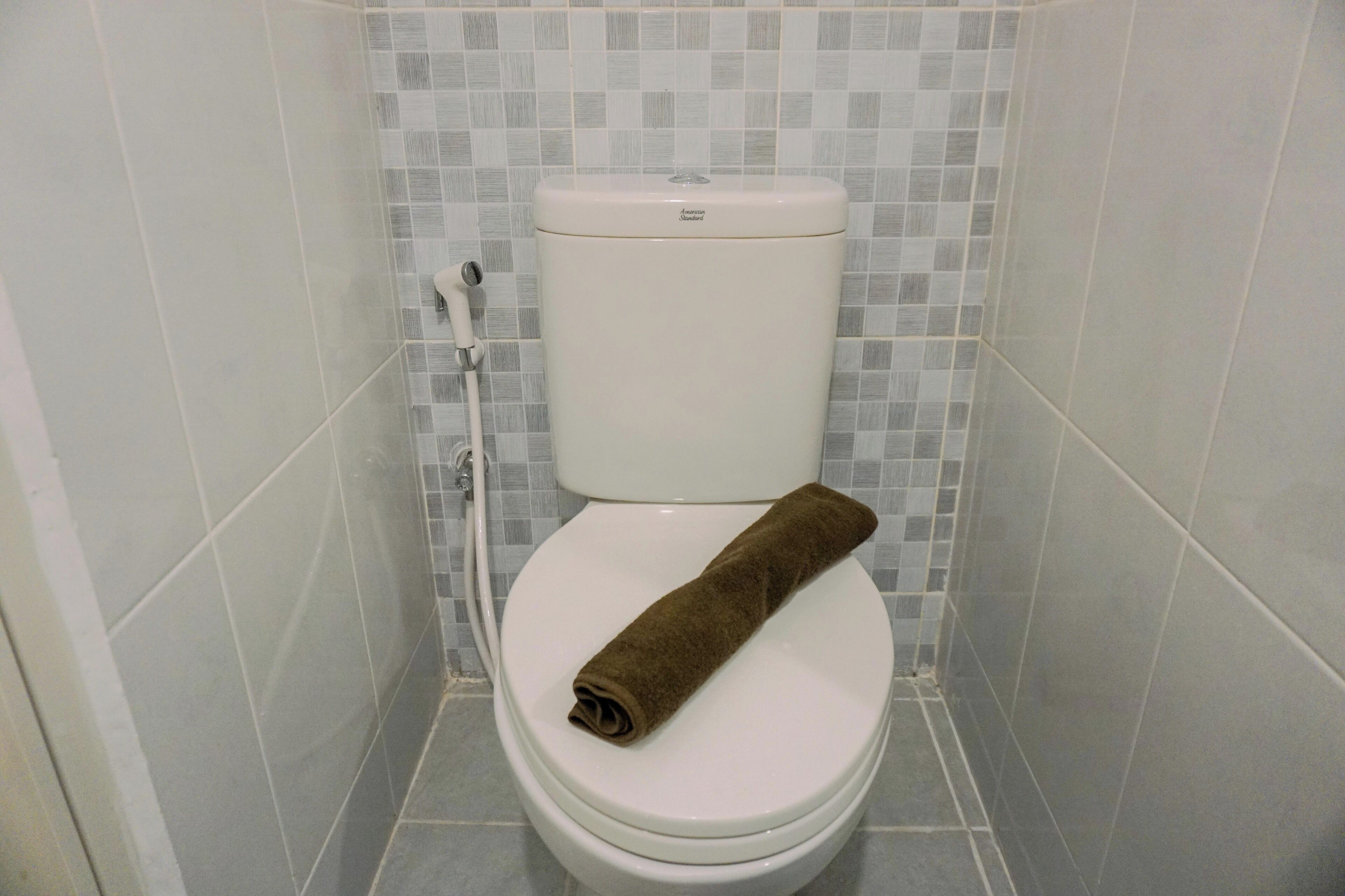 A toilet with a brown towel on the seat, a flush handle, and a tiled wall.