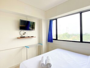 A hotel room with a bed, a TV mounted on the wall, a window with curtains, and a view of the outside. - Spacious And Comfy 2Br With Extra Room At Meikarta Apartment (Cikarang)
