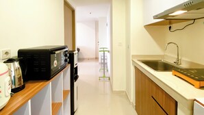 A kitchen with a microwave, toaster, and sink. There is a wooden shelf and a white countertop. - Spacious And Comfy 2Br With Extra Room At Meikarta Apartment (Cikarang)