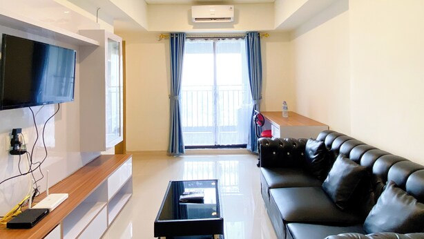 A modern living room with a flat-screen TV, a leather sofa, a coffee table, and a balcony with a view. - Spacious And Comfy 2Br With Extra Room At Meikarta Apartment (Cikarang)