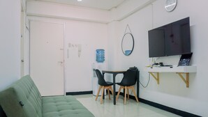 A small, clean room with a green sofa, a table with two chairs, a water dispenser, and a TV mounted on the wall. - Cozy And Comfort Living 2Br Green Bay Pluit Apartment (Jakarta)
