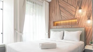 A modern bedroom with a large bed, white bedding, and a wooden accent wall. - Gorgeous And Comfortable 1Br Sudirman Suites Apartment (Jakarta)