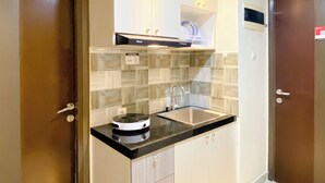 A compact kitchen with a black countertop, a built-in stove, and a sink. There are white cabinets and a small shelf above the sink. - Cozy And Comfort 2Br At Pollux Chadstone Apartment (Cikarang)