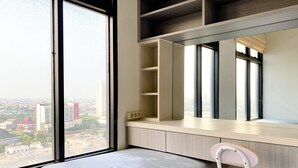 A modern room with a large window, a built-in bench, a wooden desk, and a chair. - Cozy And Comfort 2Br At Pollux Chadstone Apartment (Cikarang)