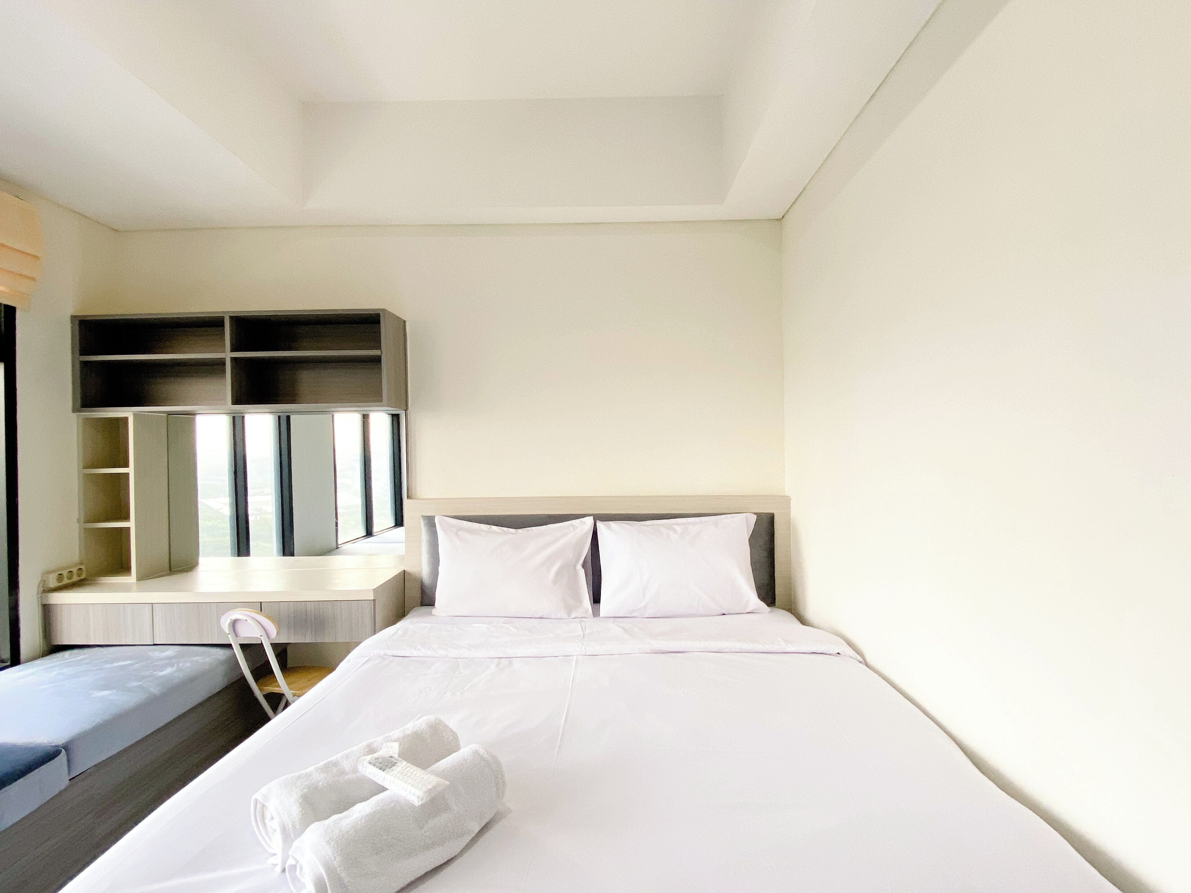 A hotel room with a bed, a seating area with a chair, a built-in shelf, and a mirror.