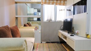 A compact living space with a sofa, a television, a radiator, and a small kitchenette area.