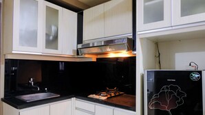 A compact kitchen with white cabinets, a stainless steel range hood, a black countertop, and a refrigerator with a flower decal.