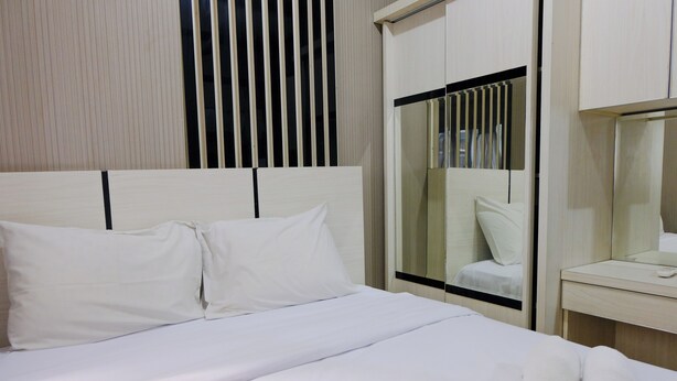 A hotel room with a neatly made bed, a wooden headboard, a mirror, and a wooden wardrobe with a black frame.