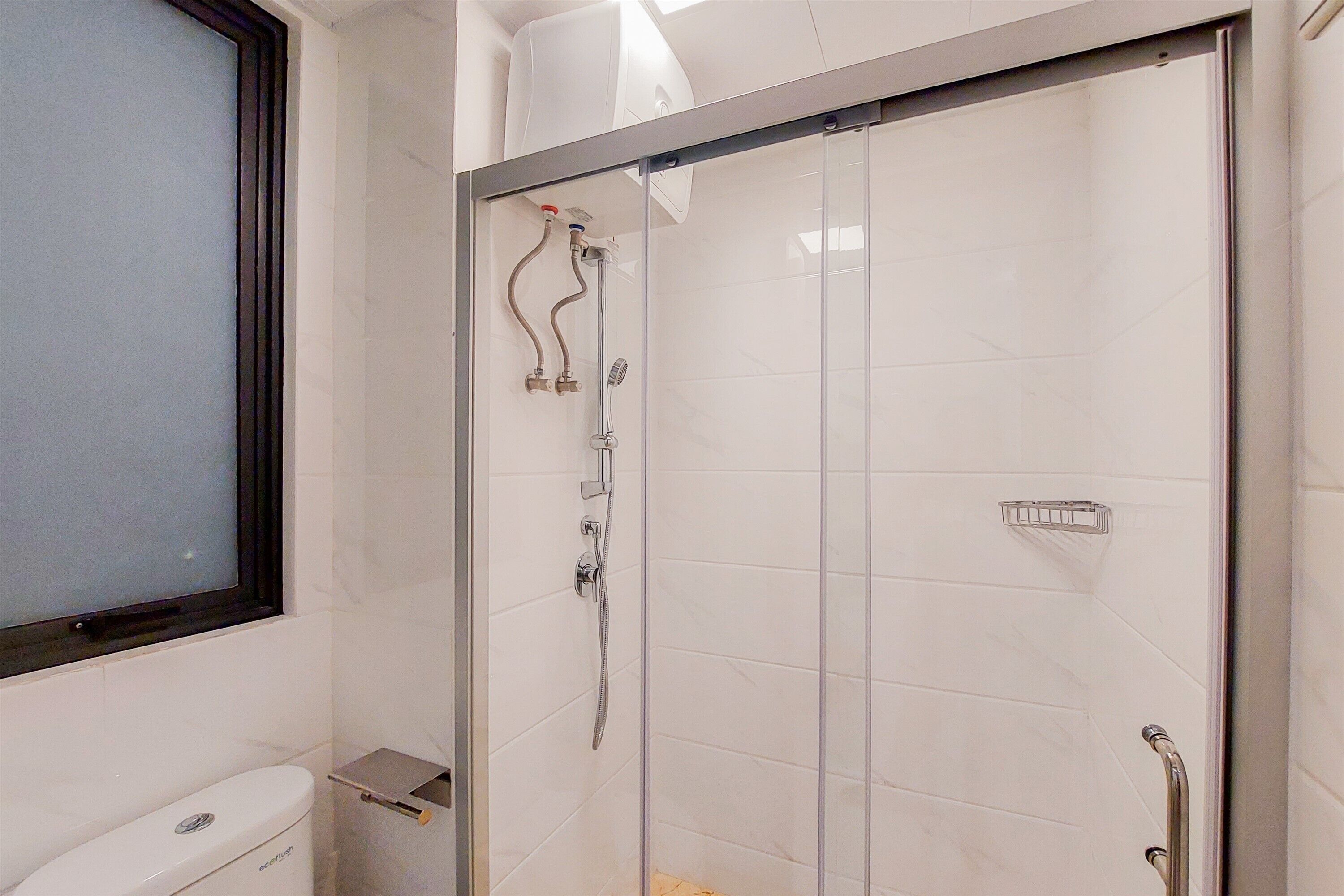 A modern bathroom with a glass shower enclosure, white tiles, and a window.