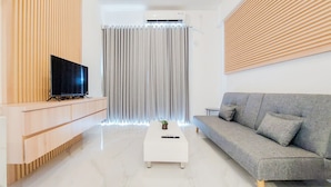 Een moderne woonkamer met een flatscreen televisie op een houten dressoir, een grijze bank en een witte salontafel met een afstandsbediening.