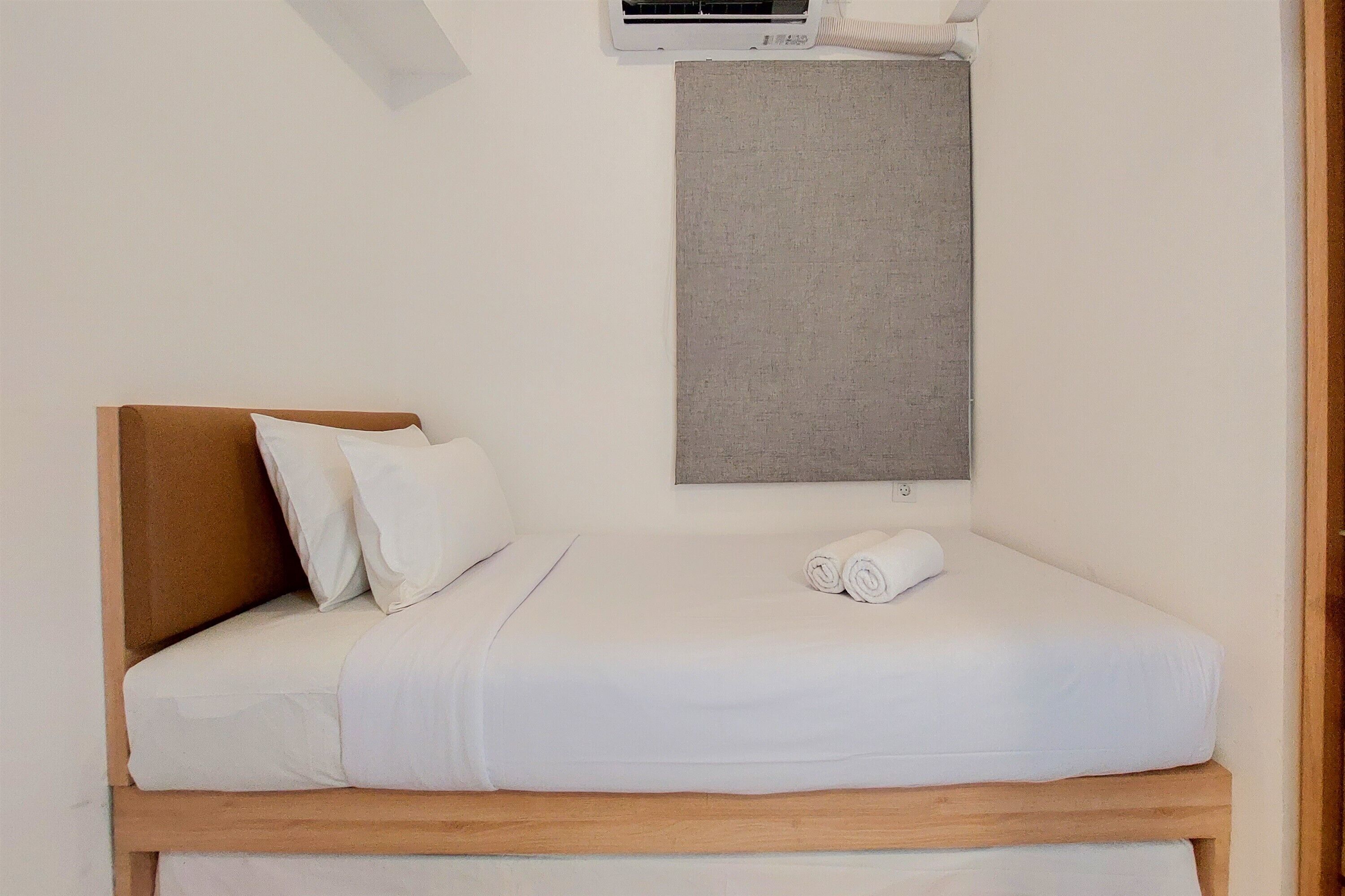A neatly made bed with white linens and a wooden headboard, a gray wall hanging above, and an air conditioning unit on the wall.