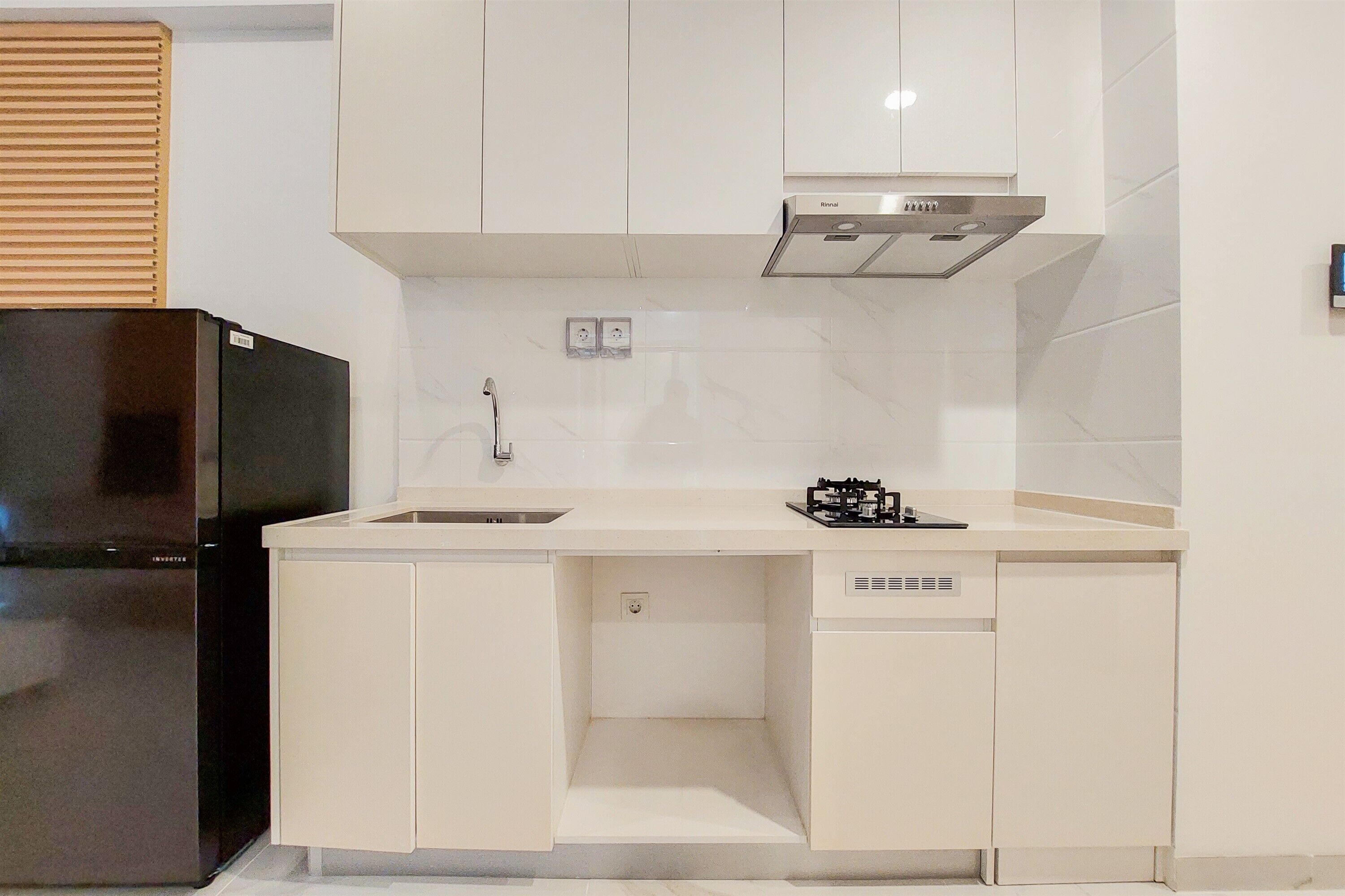 A compact kitchen with white cabinetry, a black refrigerator, a built-in dishwasher, and a stainless steel range hood.