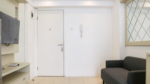A room with a closed door, a television mounted on the wall, a sofa, and a small desk with drawers. - Comfort And Modern 2Br At Bassura City Apartment (Jakarta)