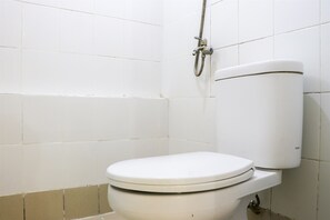 A white toilet with a tank and a shower head mounted on the wall.