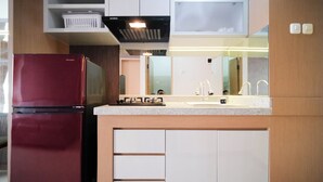 A compact kitchen with a red refrigerator, a gas stove, and a sink. - Spacious 2Br Combine Unit At Bale Hinggil Apartment (Surabaya)