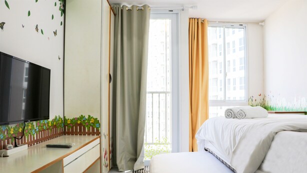 Een slaapkamer met een bed, een tv aan de muur, een raam met gordijnen en een klein balkon.