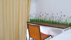 Een kamer met een houten bureau en een oranje stoel, een witte muur met een bloemenmural en een beige gordijn.