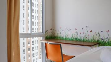 A hotel room with a bed, a desk with a chair, a window with curtains, and a wall with a floral and butterfly mural.