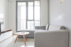 A modern living room with a grey sofa, a small round wooden table, and a TV on a white cabinet.