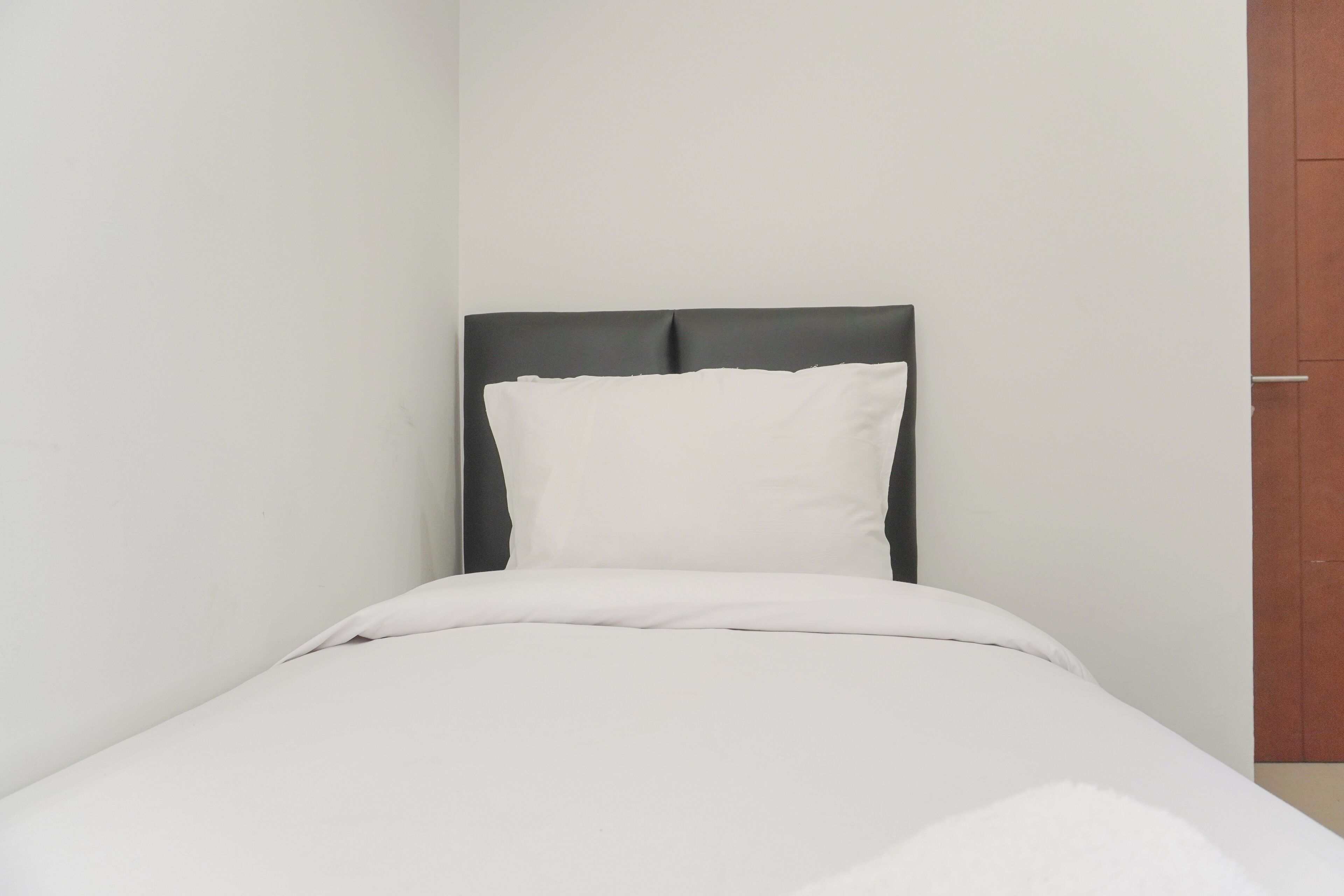 Una cama individual con cabecera oscura y ropa de cama blanca en una habitación minimalista.