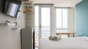 A hotel room with a bed, a TV mounted on the wall, a wardrobe, and a balcony with a view. - Best Deal And Comfort Studio Tokyo Riverside Pik 2 Apartment (Teluknaga)