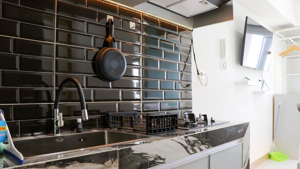 A modern kitchen with black tiled backsplash, stainless steel appliances, and a marble countertop. - Best Deal And Comfort Studio Tokyo Riverside Pik 2 Apartment (Teluknaga)