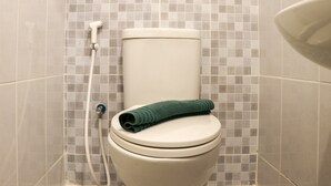 Des toilettes avec une serviette verte posée sur la cuvette, une pomme de douche et un mur carrelé.