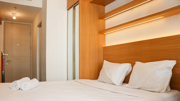 Une chambre d’hôtel avec une tête de lit en bois, un lit bien fait avec du linge de lit blanc, et une porte visible sur la gauche.
