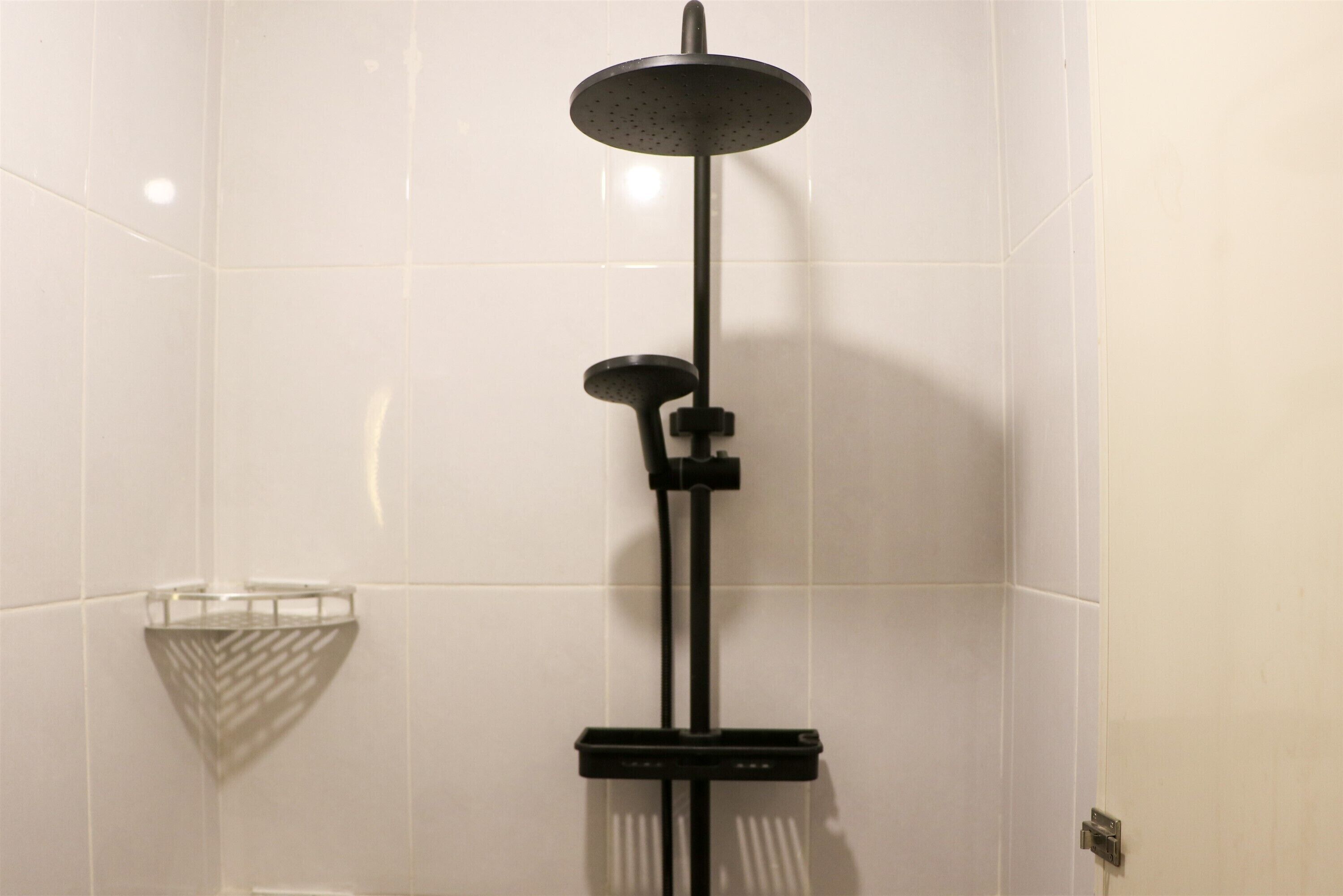 Ducha moderna con cabezal de ducha tipo lluvia y cabezal de ducha de mano, montados en un soporte negro frente a una pared de azulejos blancos.