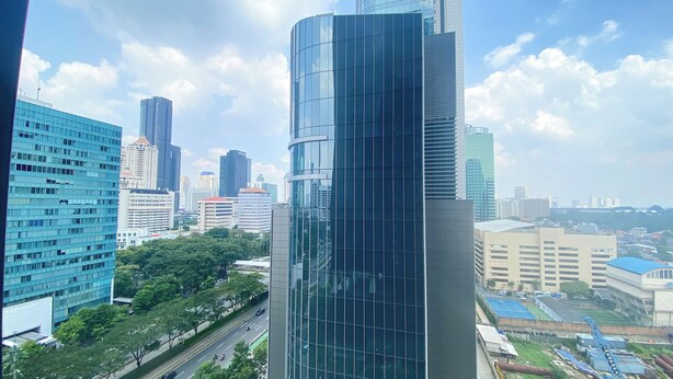 A modern high-rise building with a curved glass facade, surrounded by other skyscrapers and a highway with vehicles. - Comfort And Elegant 2Br Sudirman Suites Apartment (Jakarta)