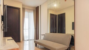 A modern hotel room with a sofa, a wooden desk, and a large mirror reflecting the room. - Comfort And Elegant 2Br Sudirman Suites Apartment (Jakarta)