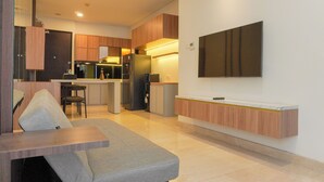 A modern kitchen with wooden cabinets, a built-in island, and a flat-screen TV mounted on the wall. - Comfort And Elegant 2Br Sudirman Suites Apartment (Jakarta)