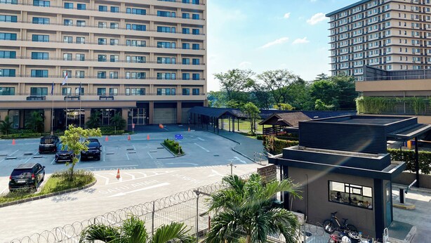 Ein mehrstöckiges Hotel mit Parkplatz, überdachtem Gang und einem kleinen Gebäude mit Fahrradständer.
