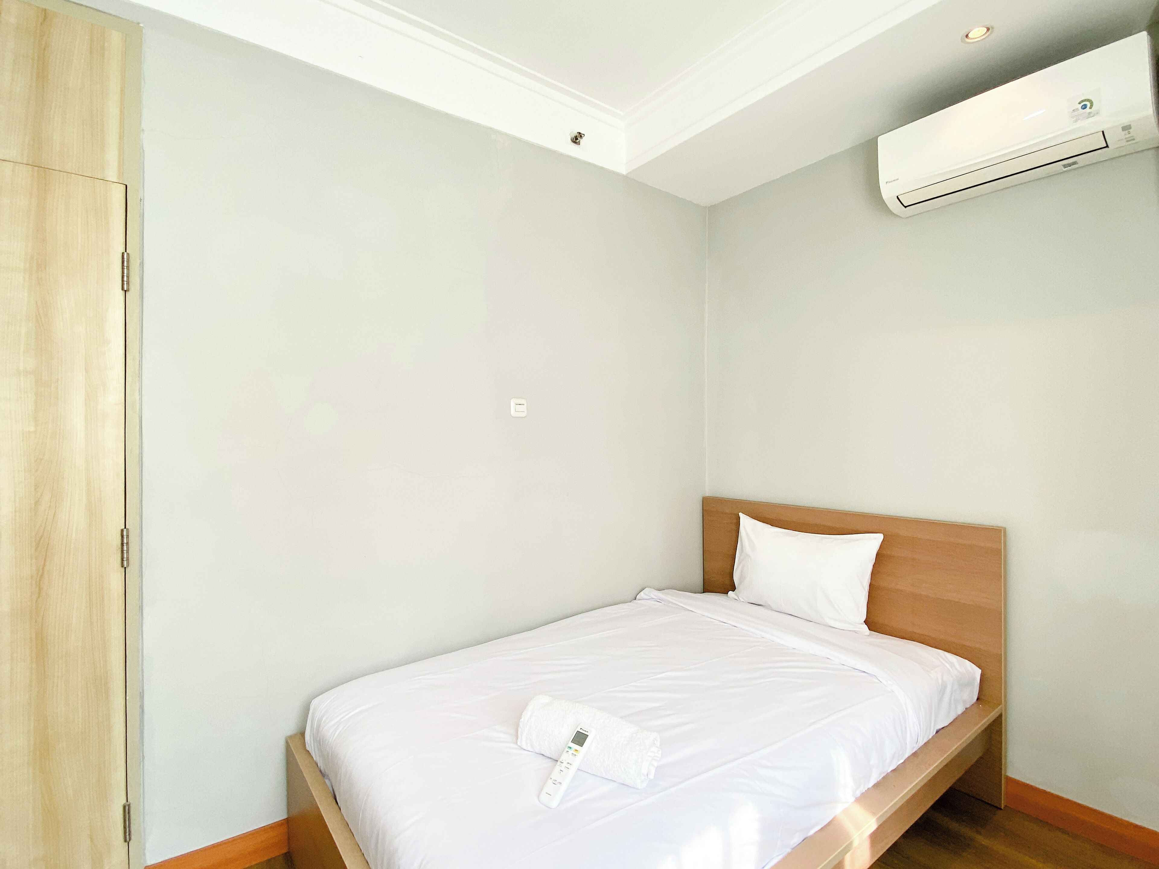 A neatly made bed with white linens and a white pillow, a wooden headboard, and a wall-mounted air conditioning unit.