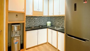 Eine kleine Küche mit weißen Schränken, einer schwarzen Küchenrückwand aus Fliesen, einem Edelstahl-Kühlschrank und einem Wasserspender.