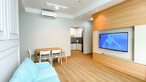 Ein modernes Wohnzimmer mit einer Couch, einem Esstisch mit Stühlen, einer Küchenzeile und einem an der Wand befestigten Fernseher.