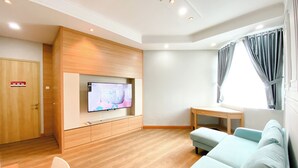 Ein modernes Wohnzimmer mit einem an einer Holzplatte montierten Flachbildfernseher, einem hellblauen Sofa, einem Holztisch und einer Holztür mit Brandschutztürschild.