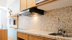 A kitchen with wooden cabinets, a countertop, a sink, and a backsplash with a speckled pattern. - Modern And New Studio At Tokyo Riverside Pik 2 Apartment (Teluknaga)