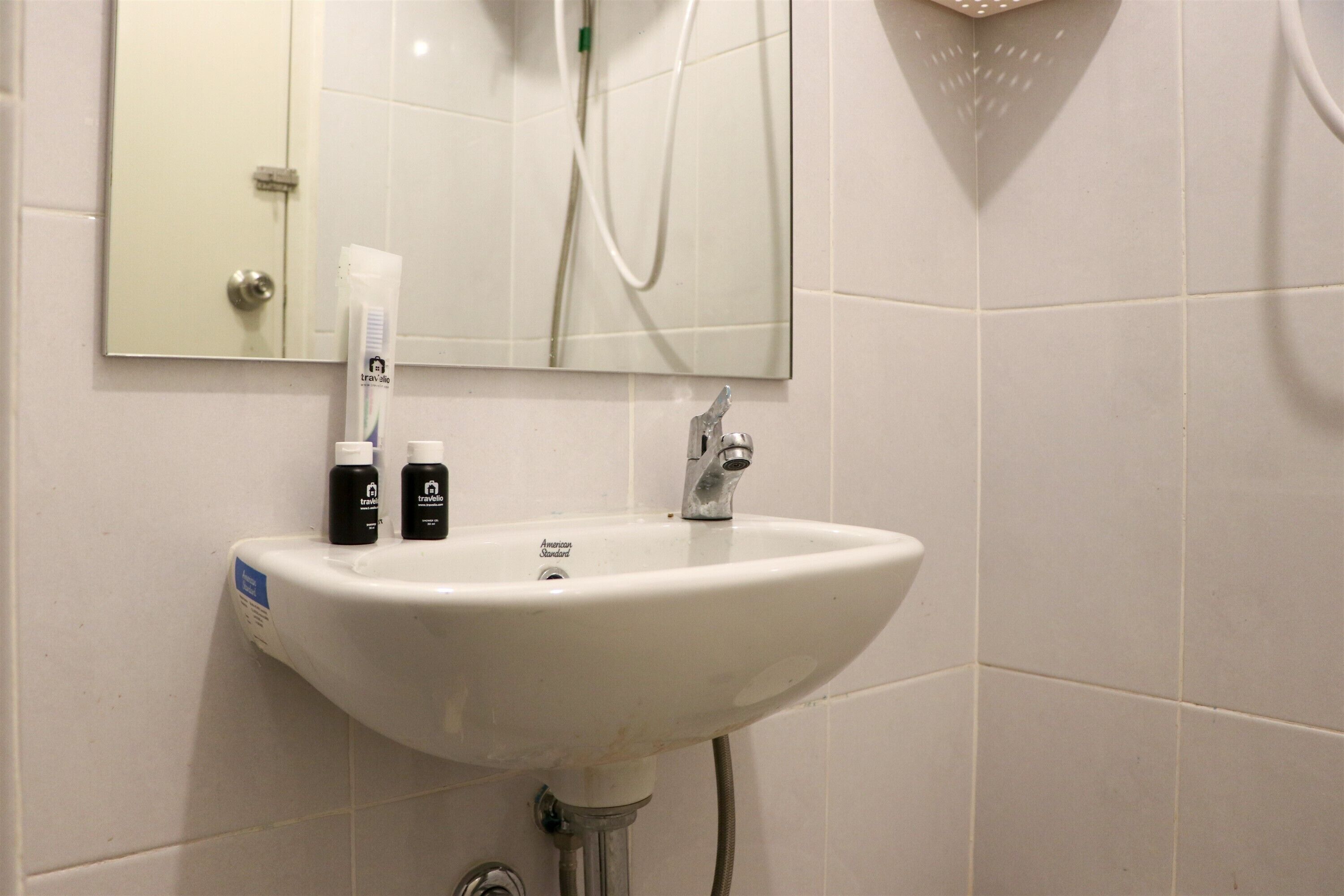 Un baño con lavamanos blanco, espejo y artículos de aseo sobre el lavamanos.