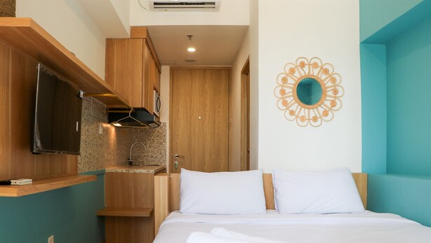A hotel room with a bed, a TV, a wooden cabinet, and a bathroom. - Modern And New Studio At Tokyo Riverside Pik 2 Apartment (Teluknaga)